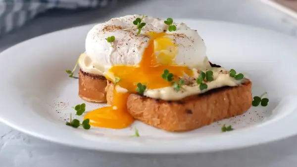 Un delicioso huevo poche con yema líquida cayendo sobre tostadas, adornado con brotes verdes y pimienta.