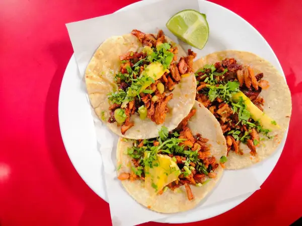 Tres deliciosos tacos al pastor, con cilantro, piña y un toque de limón, listos para disfrutar.
