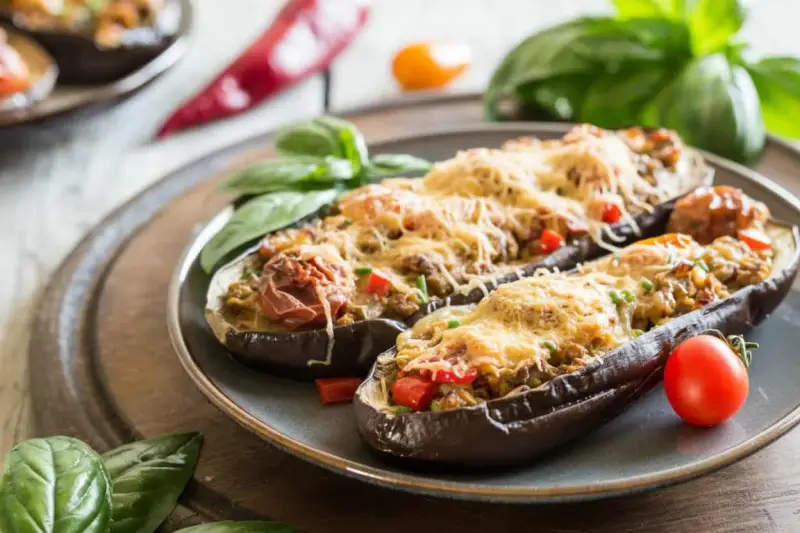 Berenjenas rellenas de atún, gratinadas con queso y decoradas con albahaca y tomate. Un plato delicioso y fácil de preparar.