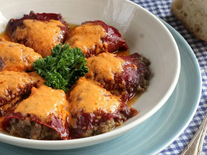 Pimientos rellenos de carne cubiertos con una cremosa salsa, decorados con perejil fresco.